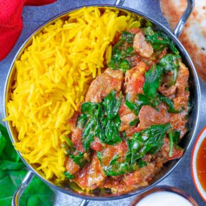 Slow Cooker Lamb Rogan Josh in a silver balti dish. Naan bread and mango accompany it.