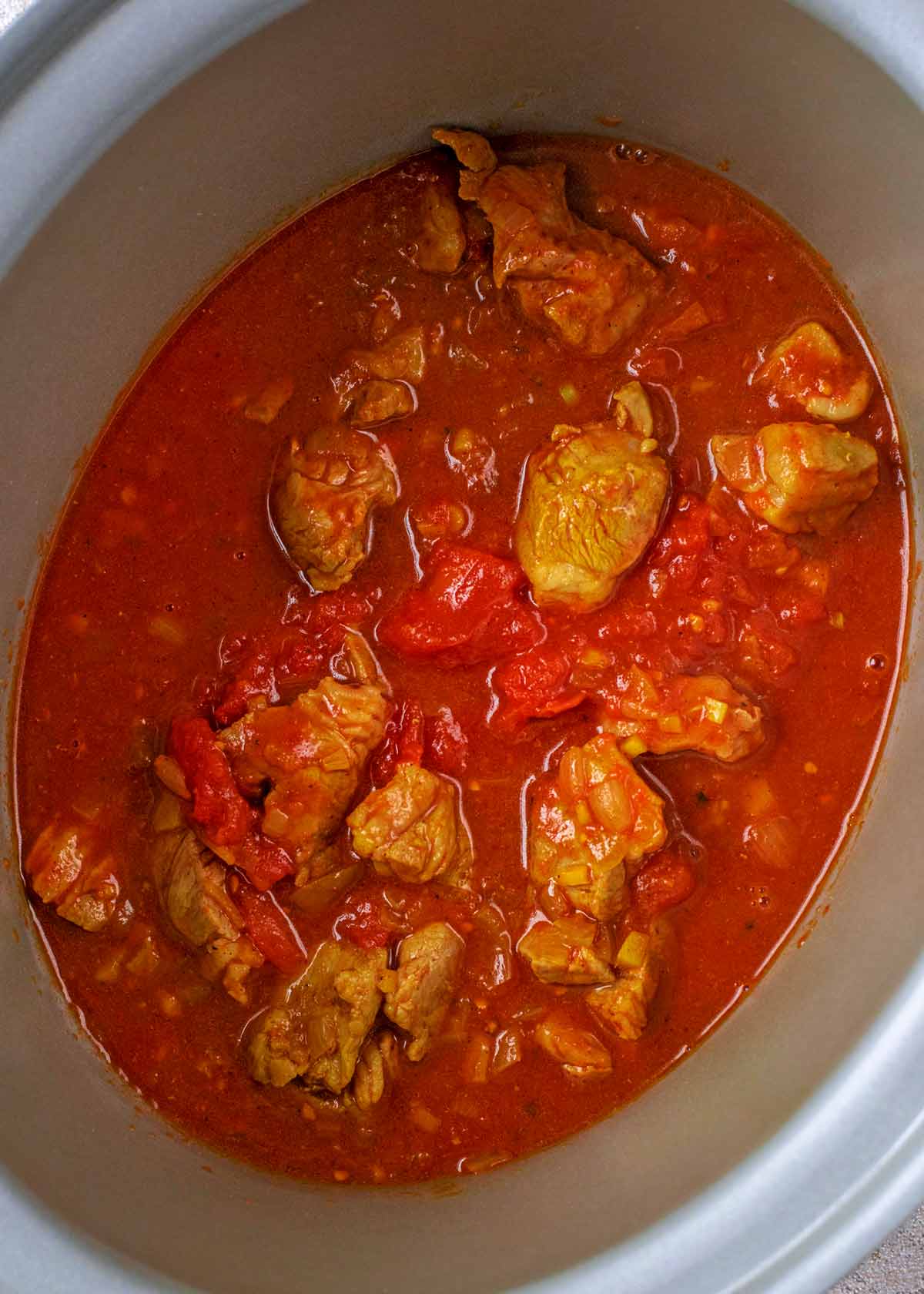 A slow cooker crockpot containing chunks of lamb in a rich tomato sauce.