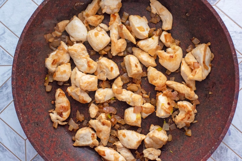 diced chicken and onions cooking in a frying pan.