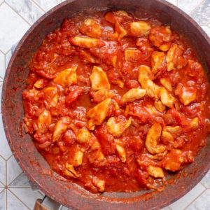 Diced chicken in a tomato sauce cooking in a frying pan