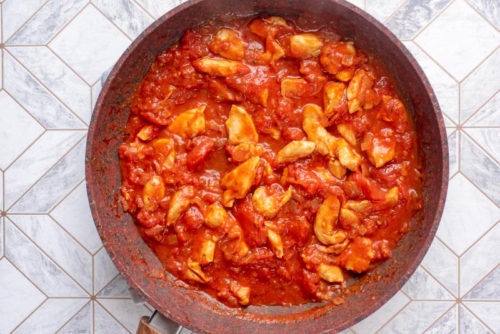Diced chicken in a tomato sauce cooking in a frying pan