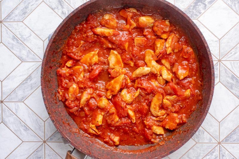 Diced chicken in a tomato sauce cooking in a frying pan.