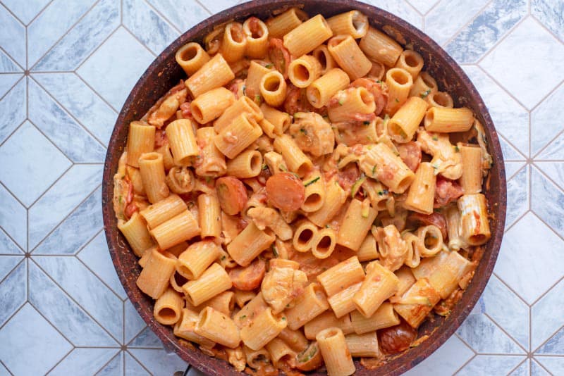 A frying pan containing pasta and chicken in a creamy tomato sauce.