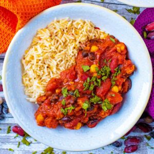 A bowl of easy three bean curry in a light blue bowl. Two towels in the background.