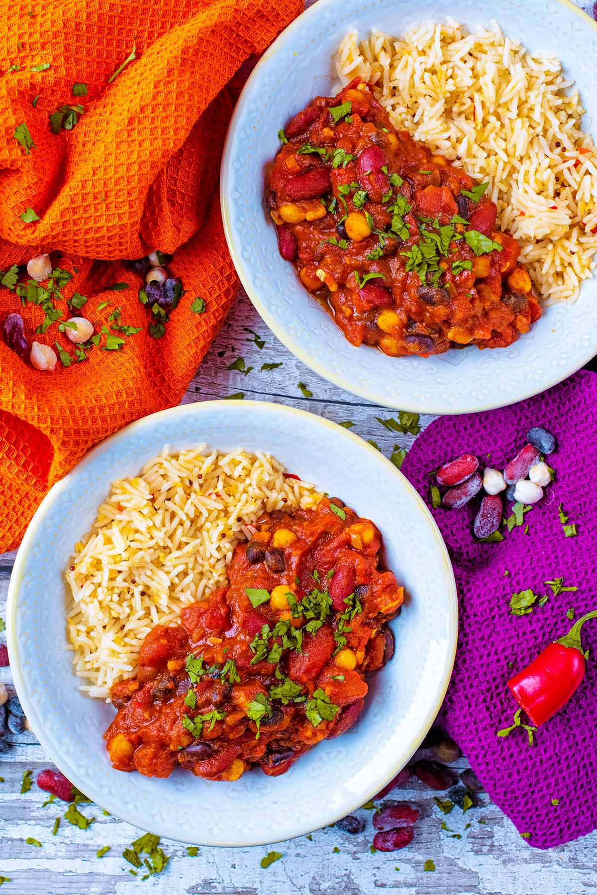 Two bowls of curry and rice with orange and purple towels next to them.