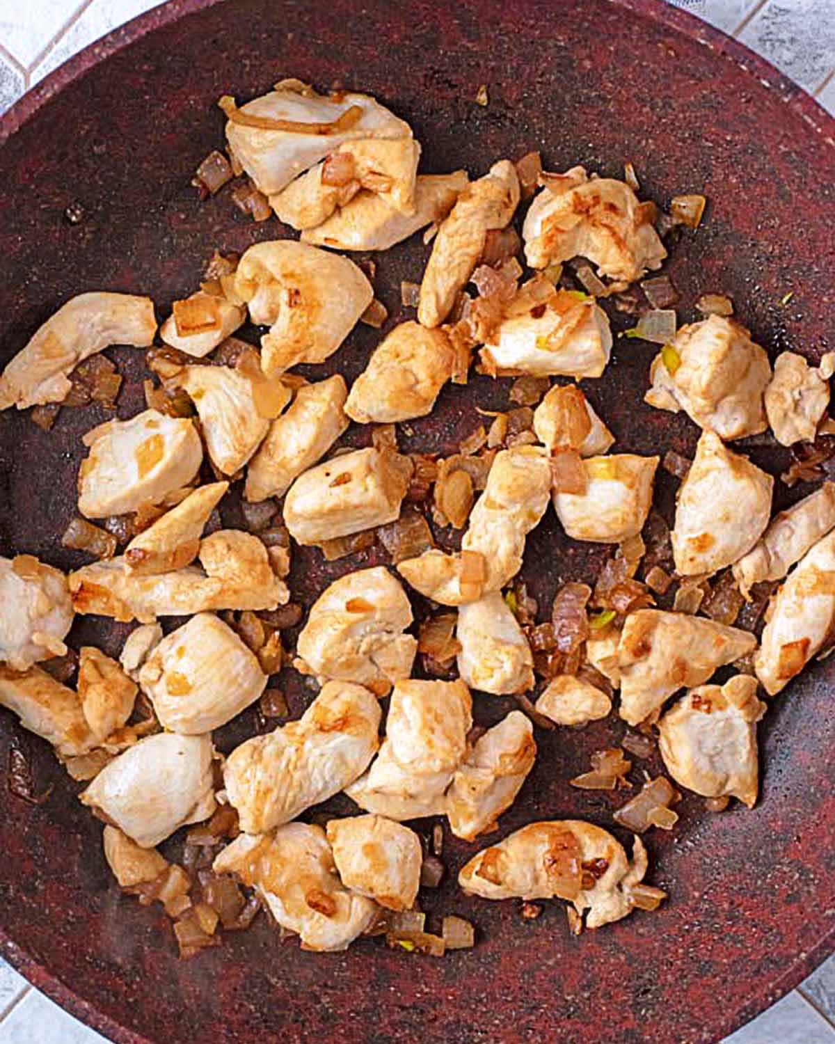 diced chicken and onions cooking in a frying pan.