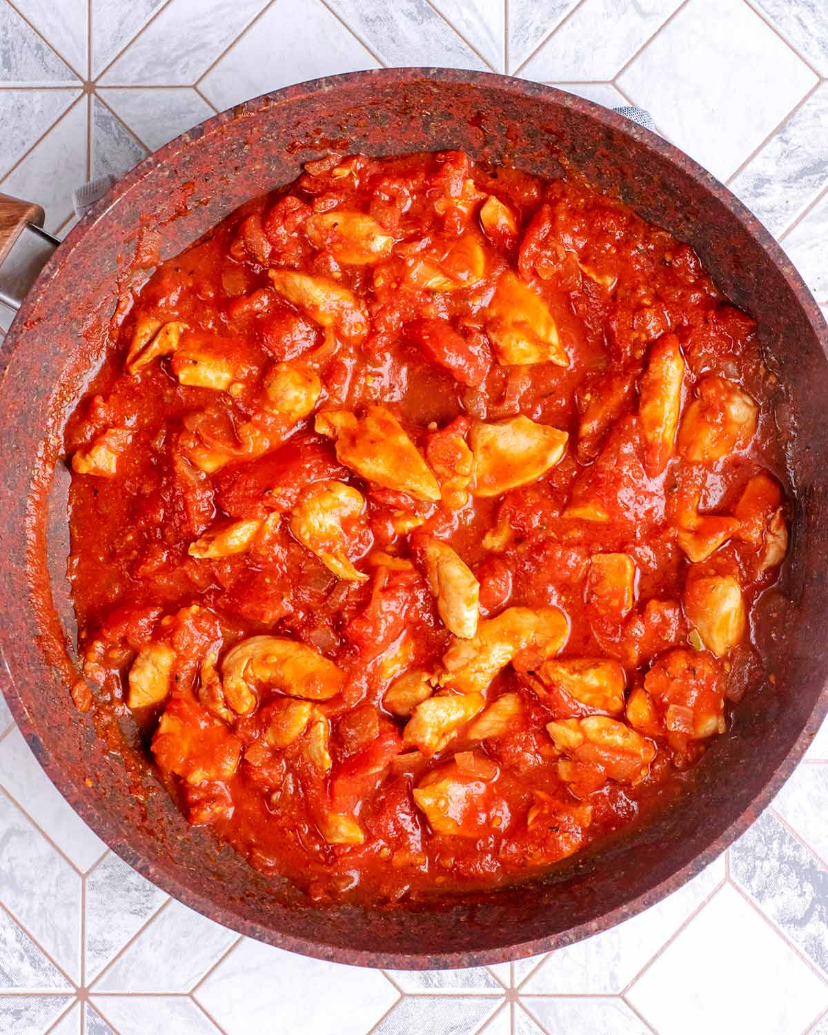 Diced chicken in a tomato sauce cooking in a frying pan.