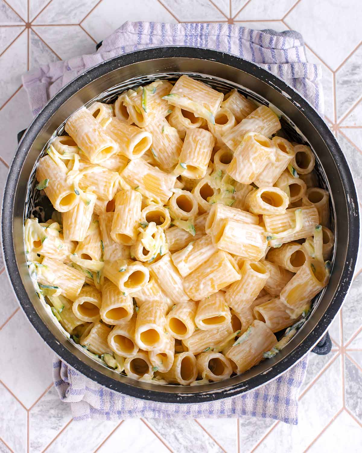 A saucepan containing cooked rigatoni pasta in a creamy sauce.