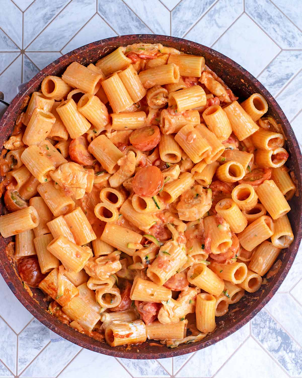 A frying pan containing pasta and chicken in a creamy tomato sauce.