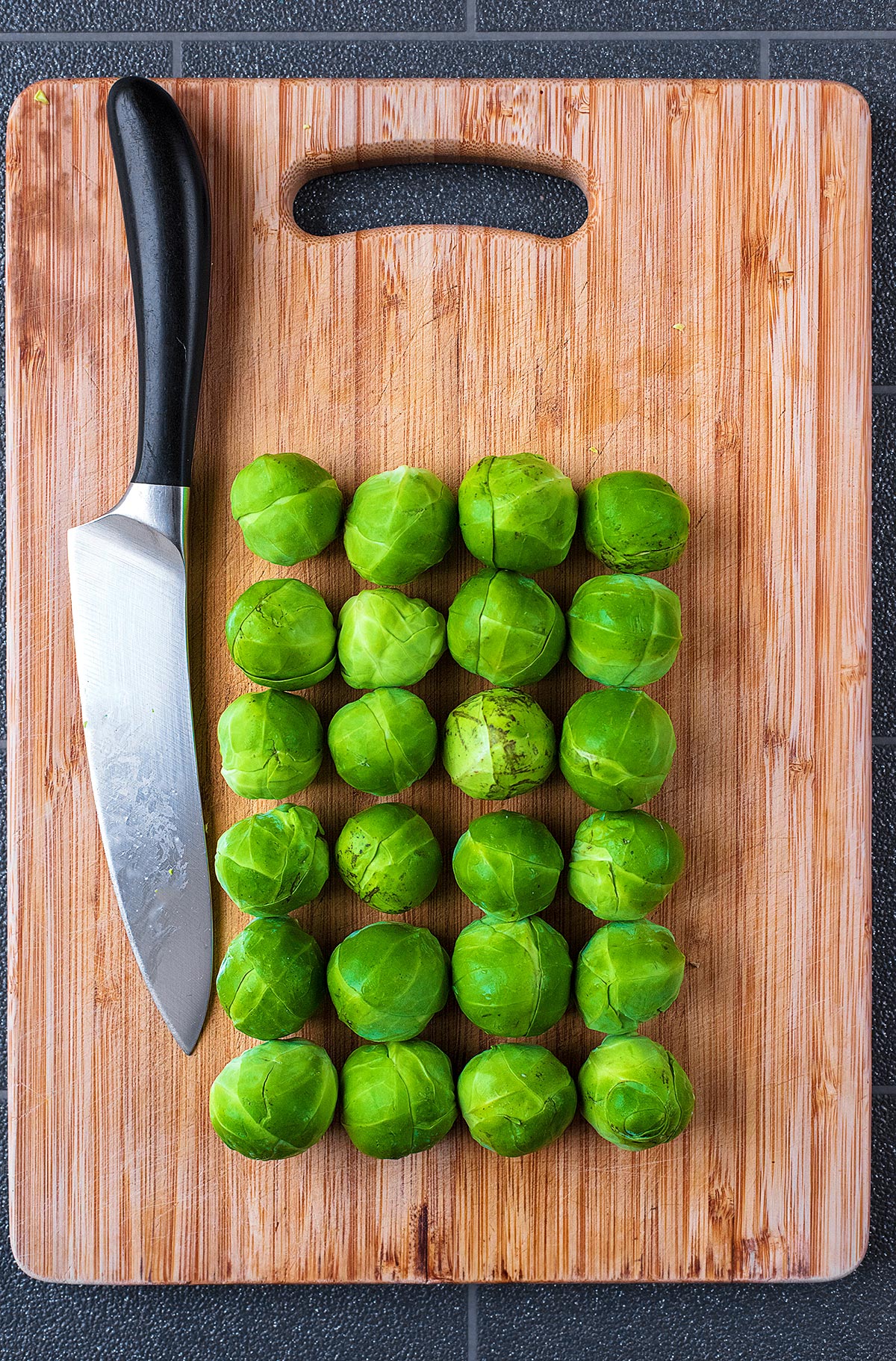 Twenty Four Brussels Sprouts on a wooden chopping board with a large knife.