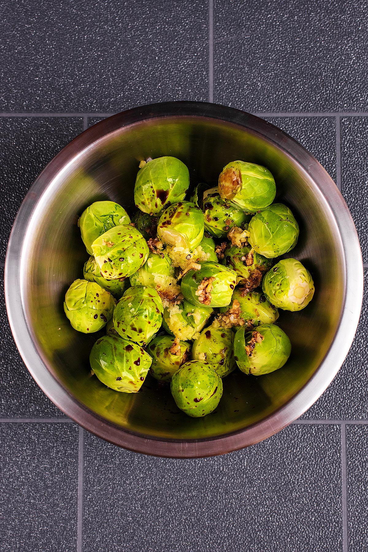 A stainless steel mixing bowl containing Brussels sprouts and balsamic vinegar.