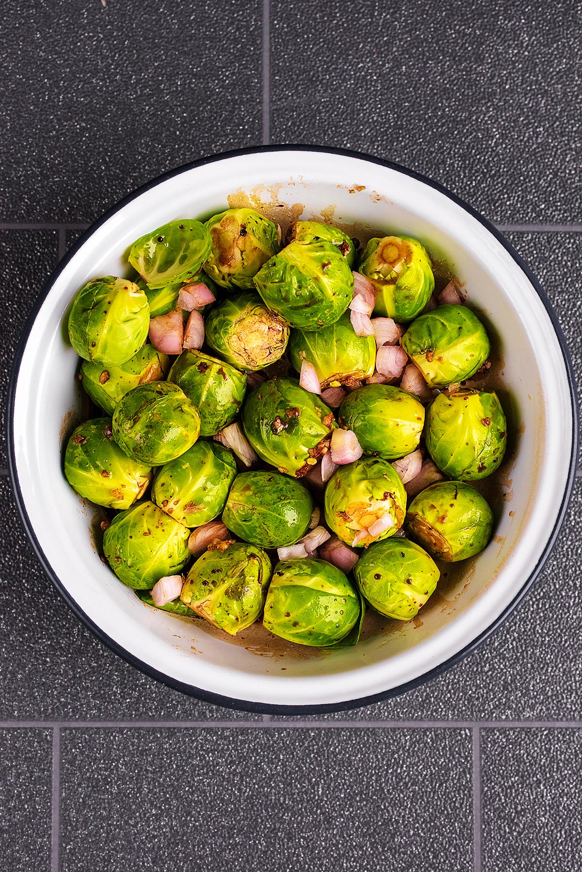 A circular baking dish containing Brussels sprouts, garlic and balsamic vinegar.
