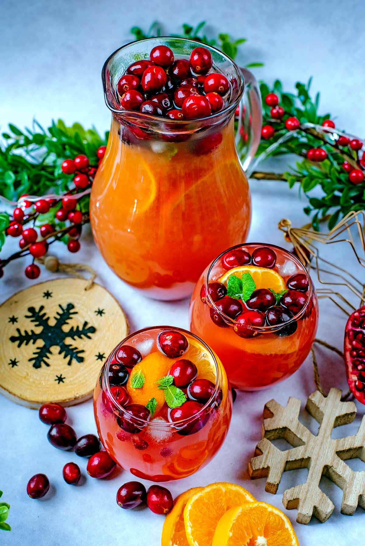 A jug and two glasses of fruit punch surrounded by Christmas decorations.