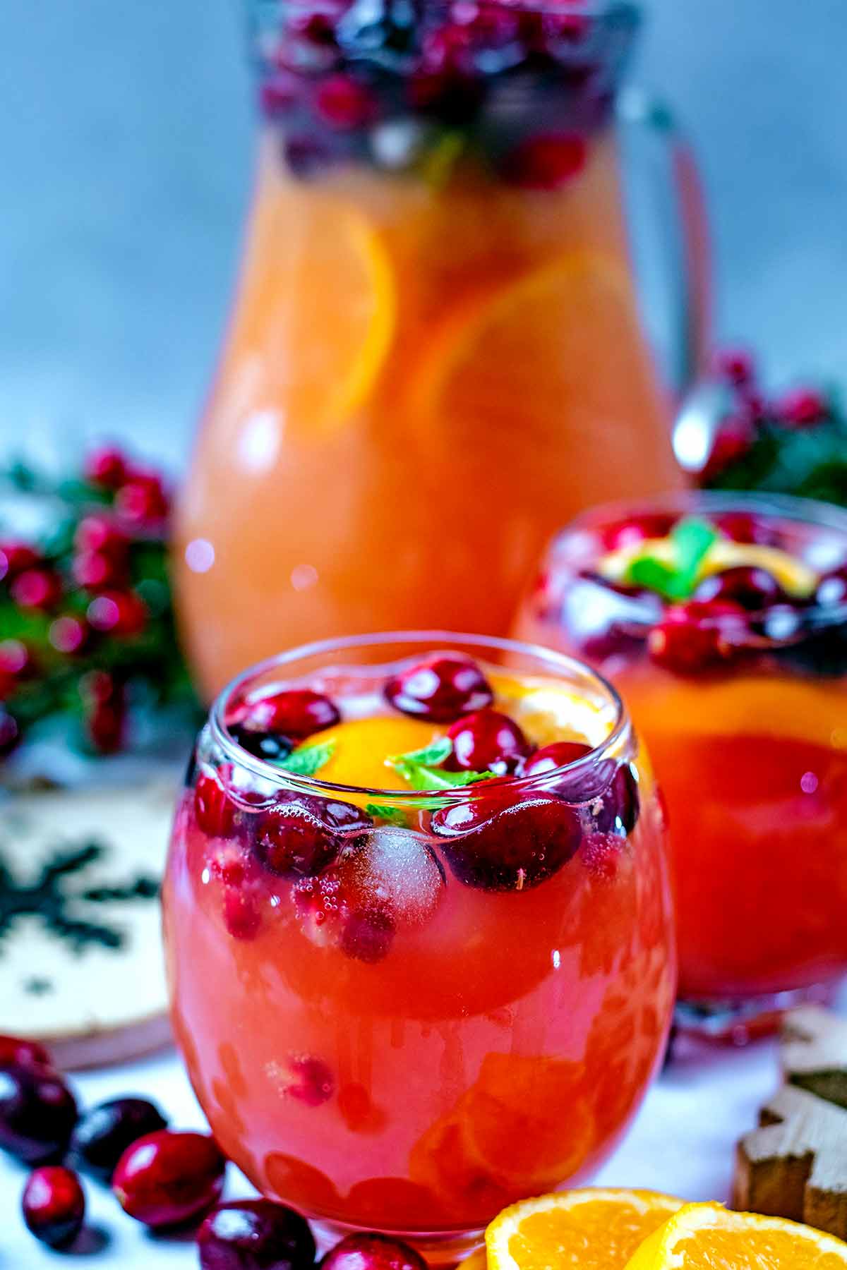 Two glasses of Christmas punch in front of a jug of more punch.