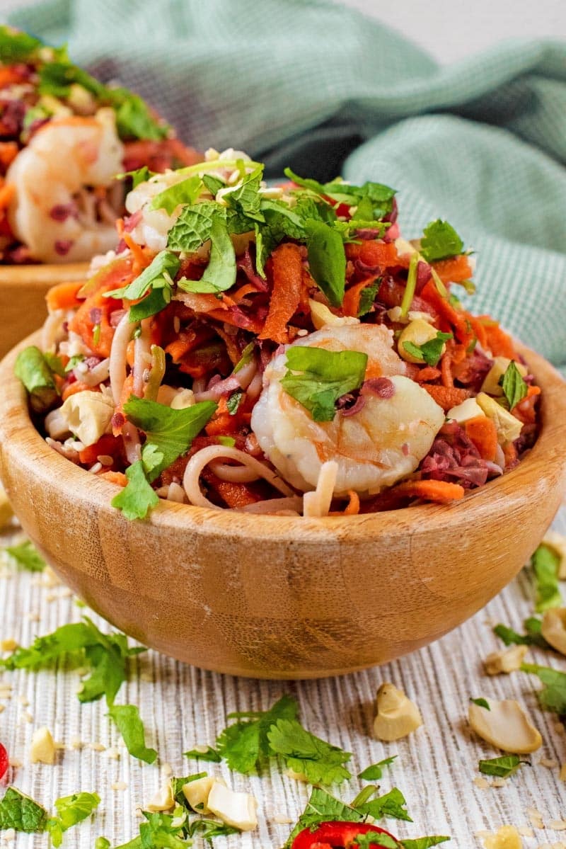 A wooden bowl of noodles topped with cooked king prawns