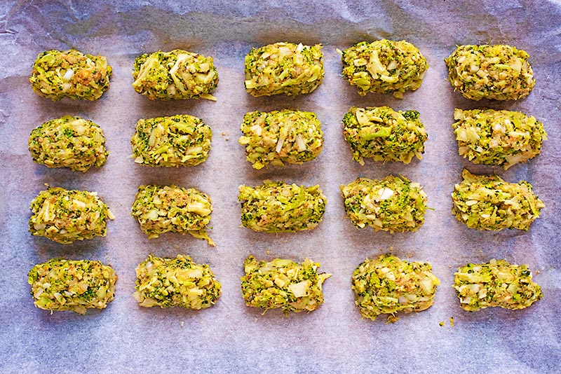 Twenty uncooked broccoli bites evenly spaced on a baking tray.