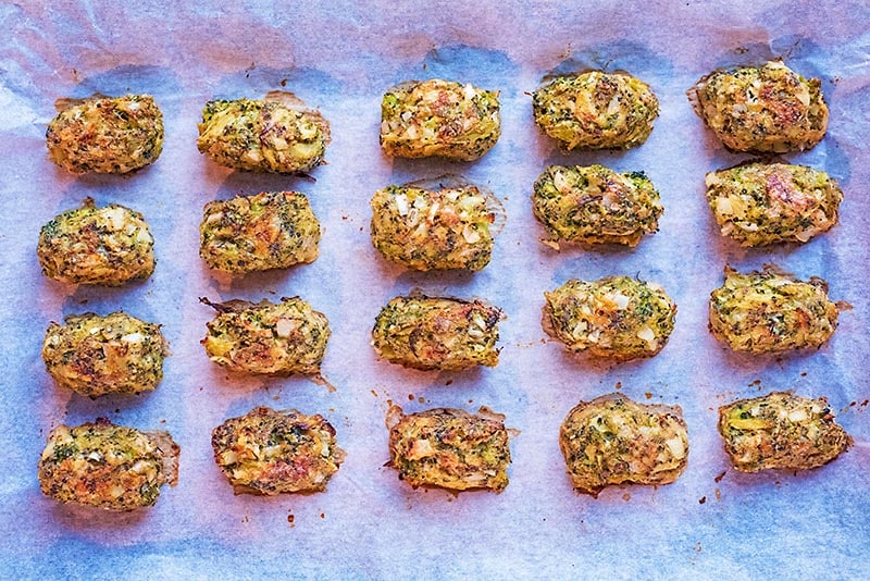 Twenty cooked broccoli bites evenly spaced on a baking tray.
