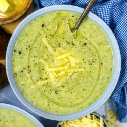 A bowl of creamy broccoli soup topped with grated cheese and a drizzle of oil.