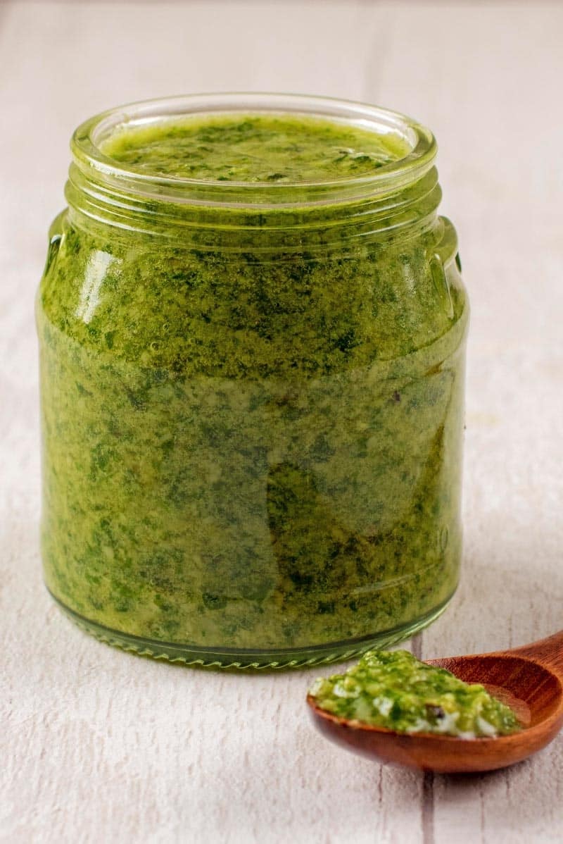 A jar of pesto oon a wooden surfave.