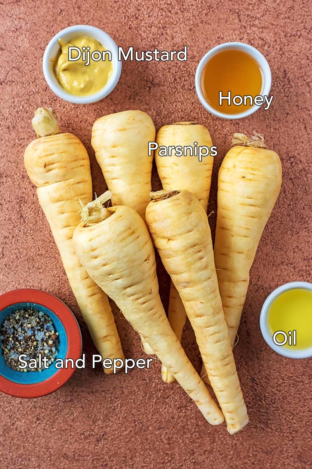 Parsnips, oil, honey, mustard and salt and pepper on a brown surface.