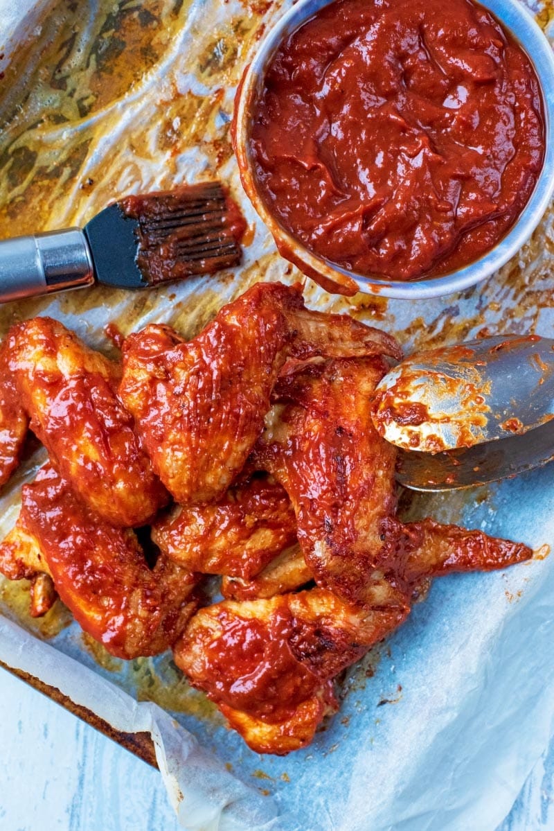 BBQ Chicken Wings on a baking tray with a pot of barbecue sauce and a basting brush.