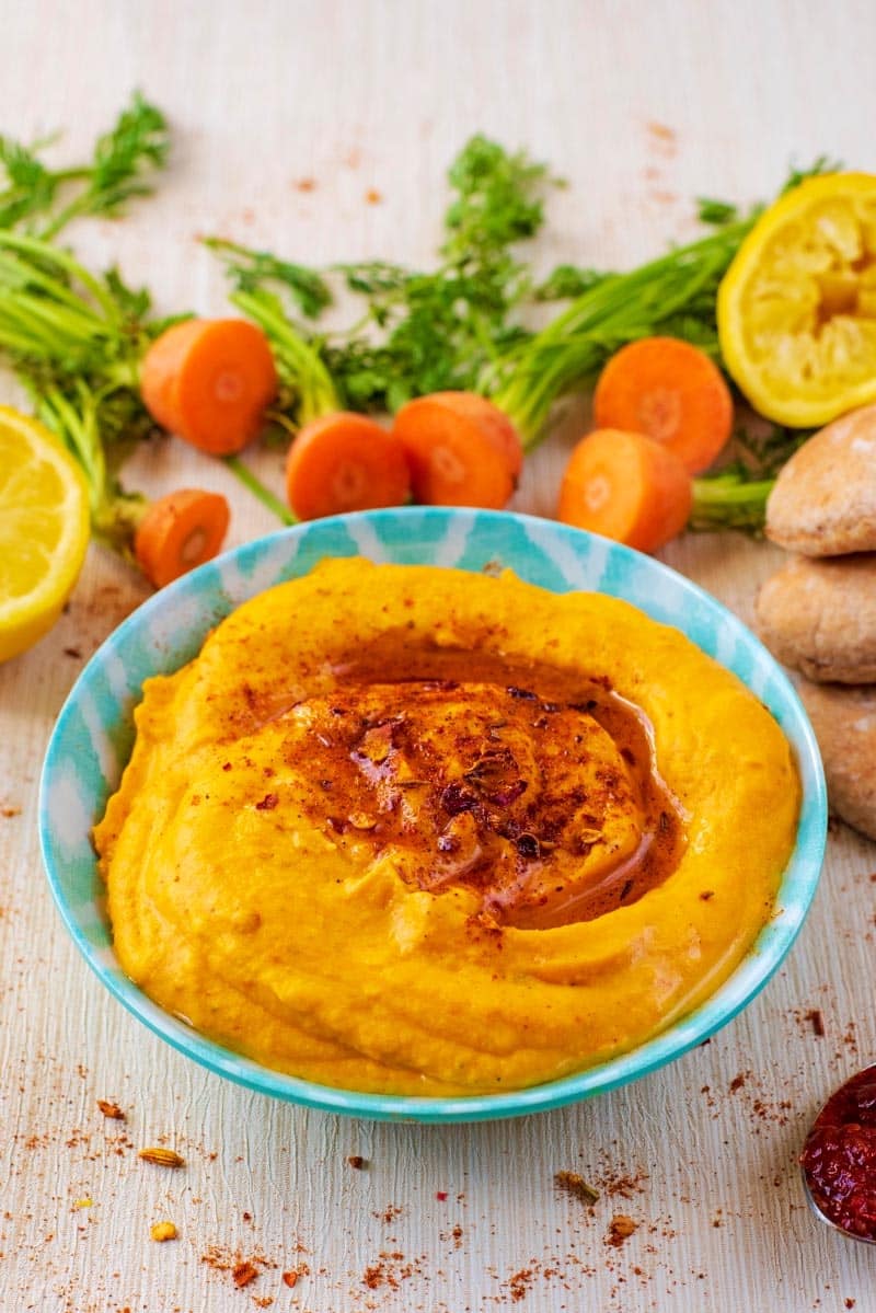 Carrot hummus topped with ras-el-hanout in front of cut carrot tops.