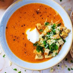 Sweet Potato and Butternut Squash Soup in a bowl topped with croutons, herbs and a dollop of cream.