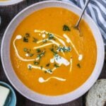 A bowl od butternut squash and sweet potato soup drizzled with cream on top.