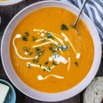 A bowl od butternut squash and sweet potato soup drizzled with cream on top.