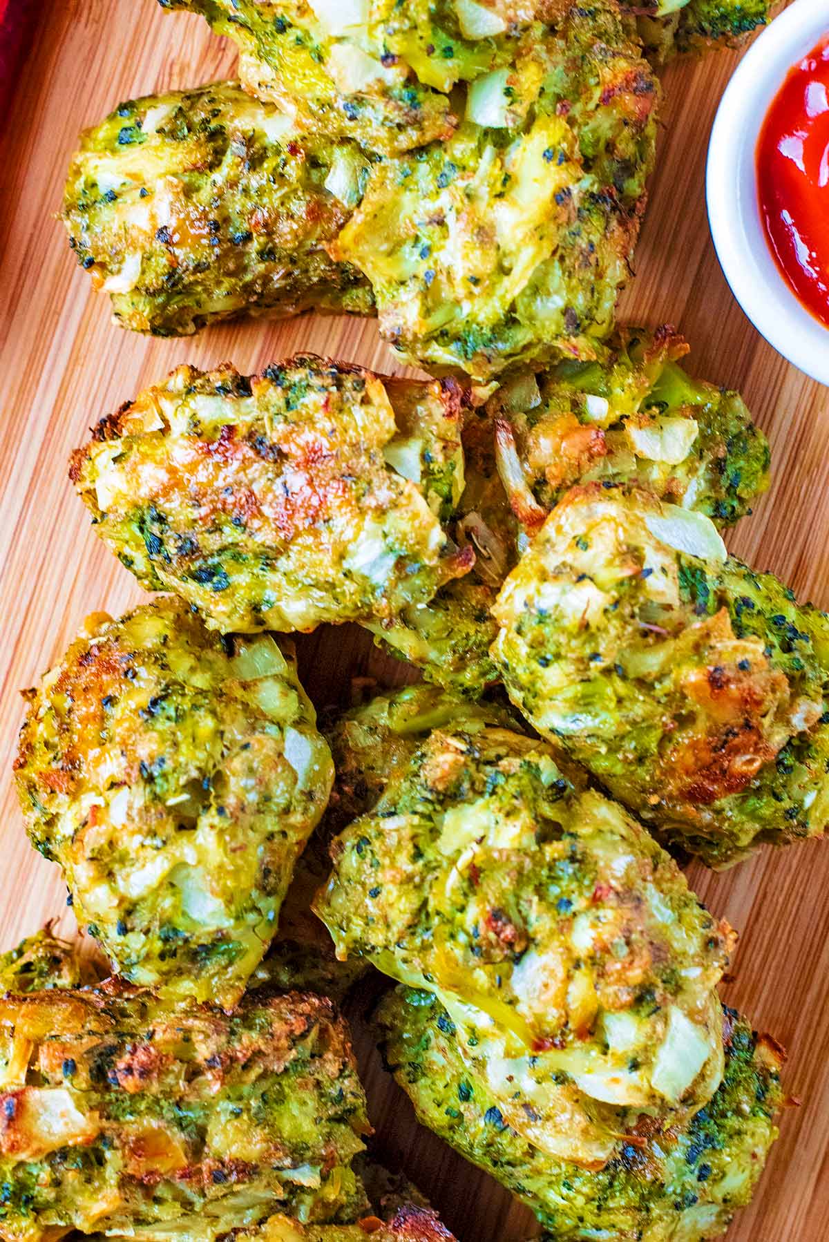 Baked Broccoli Bites stacked on a board with tomato sauce. A red towel next to them.