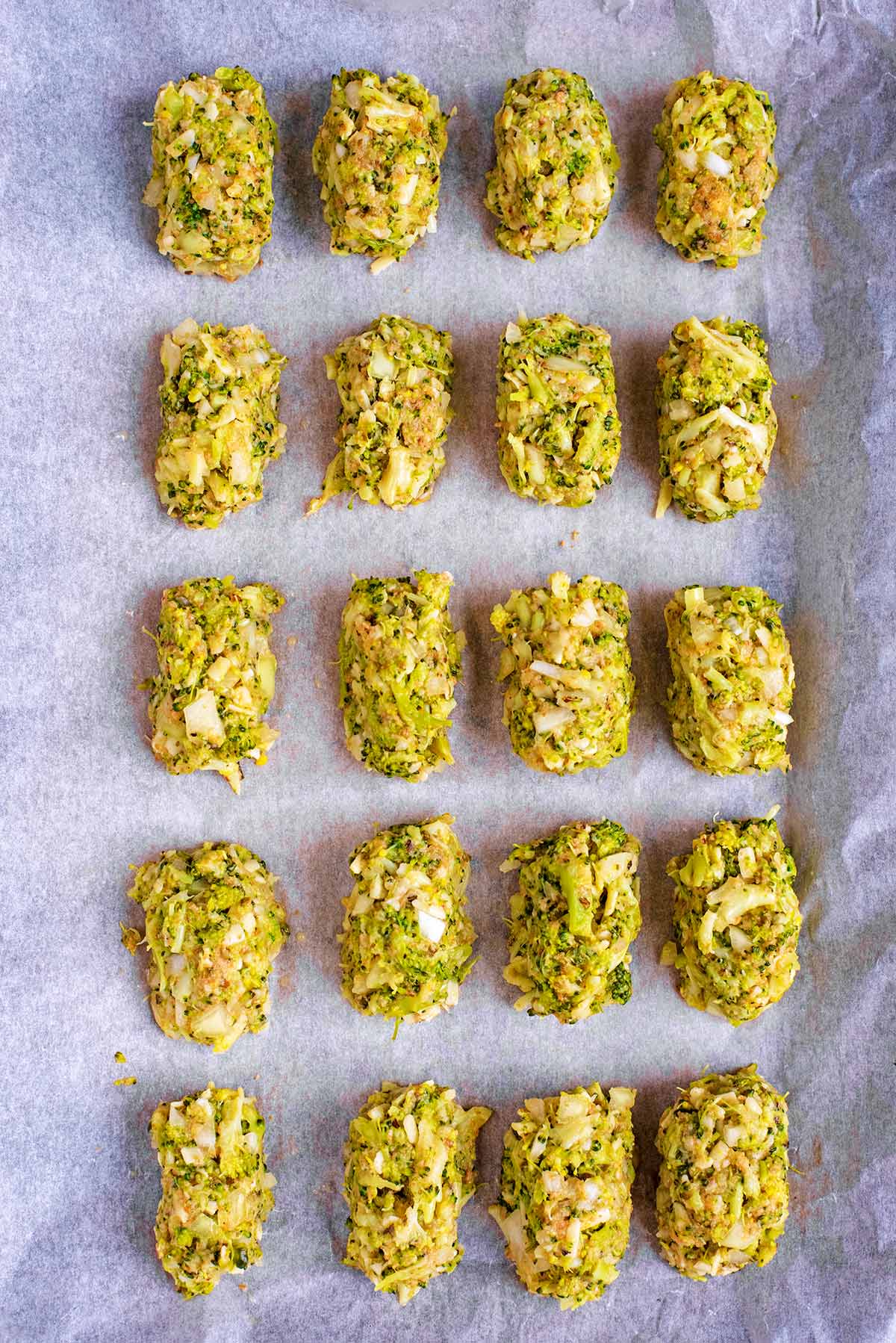 Twenty uncooked broccoli bites evenly spaced on a baking tray.