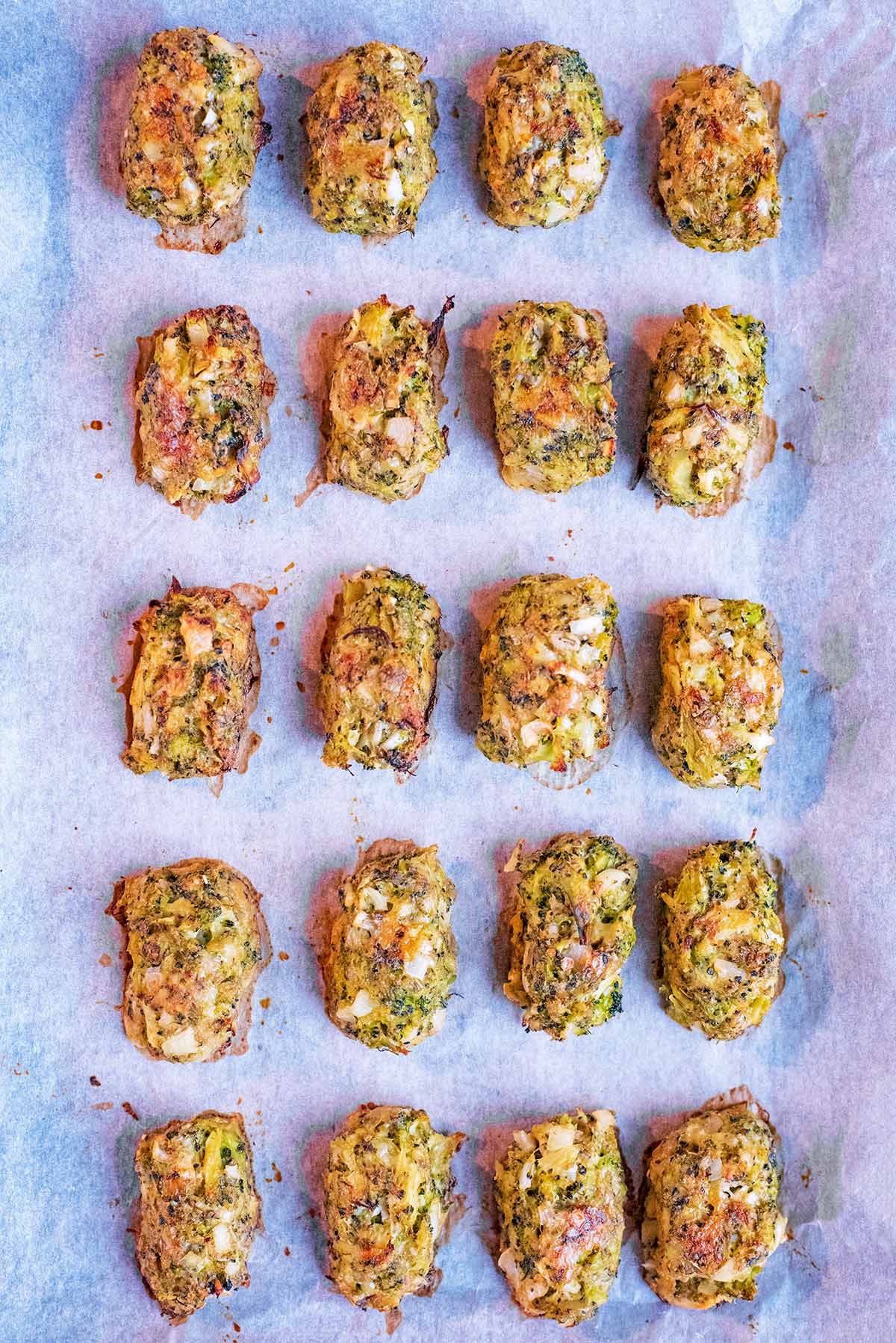 Twenty cooked broccoli bites evenly spaced on a baking tray.