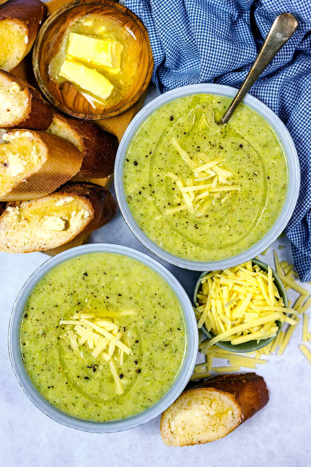 Two bowls of soup topped with grated cheese and a drizzle of oil.