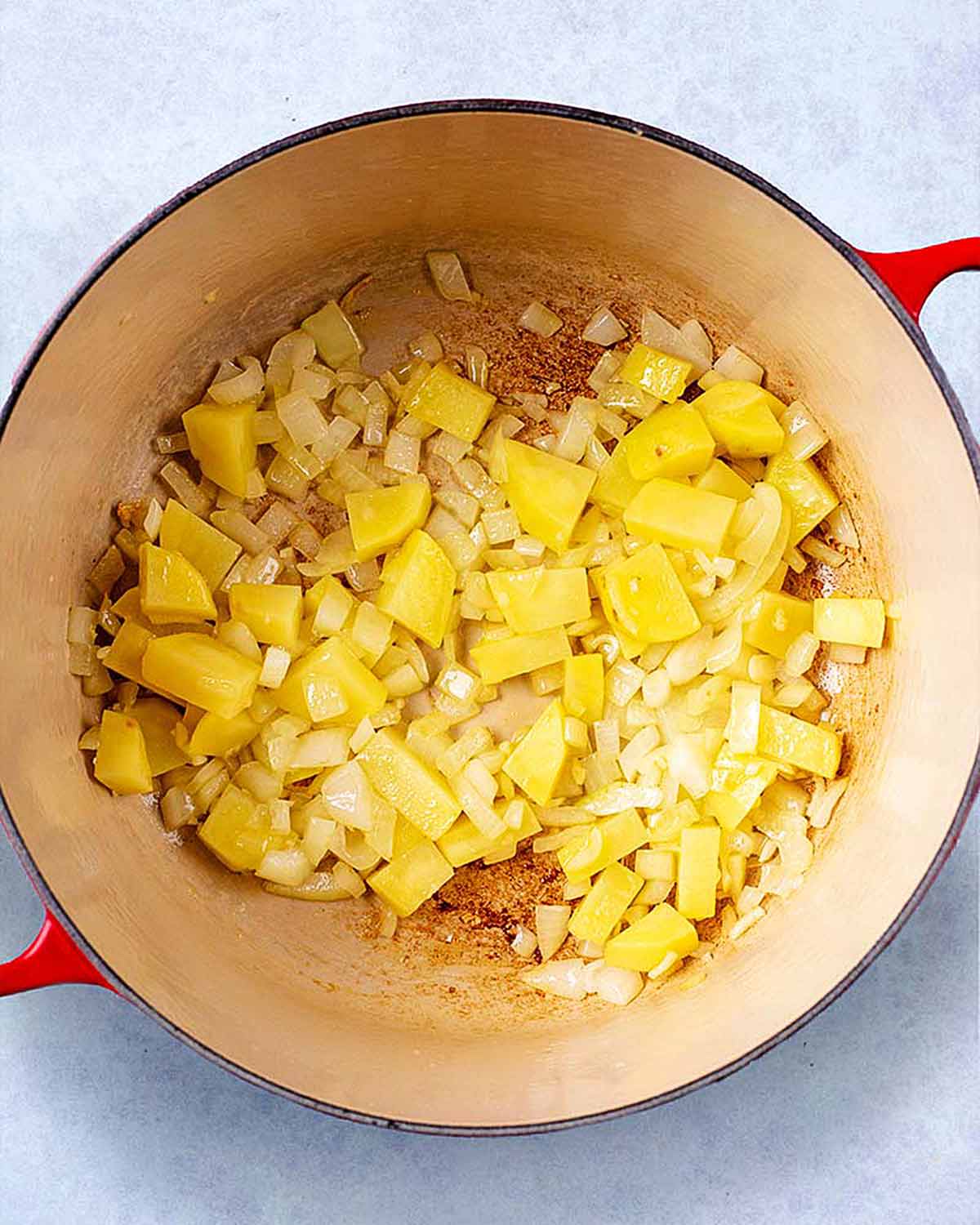 A large pan with chopped onion and chunks of potato cooking in it.