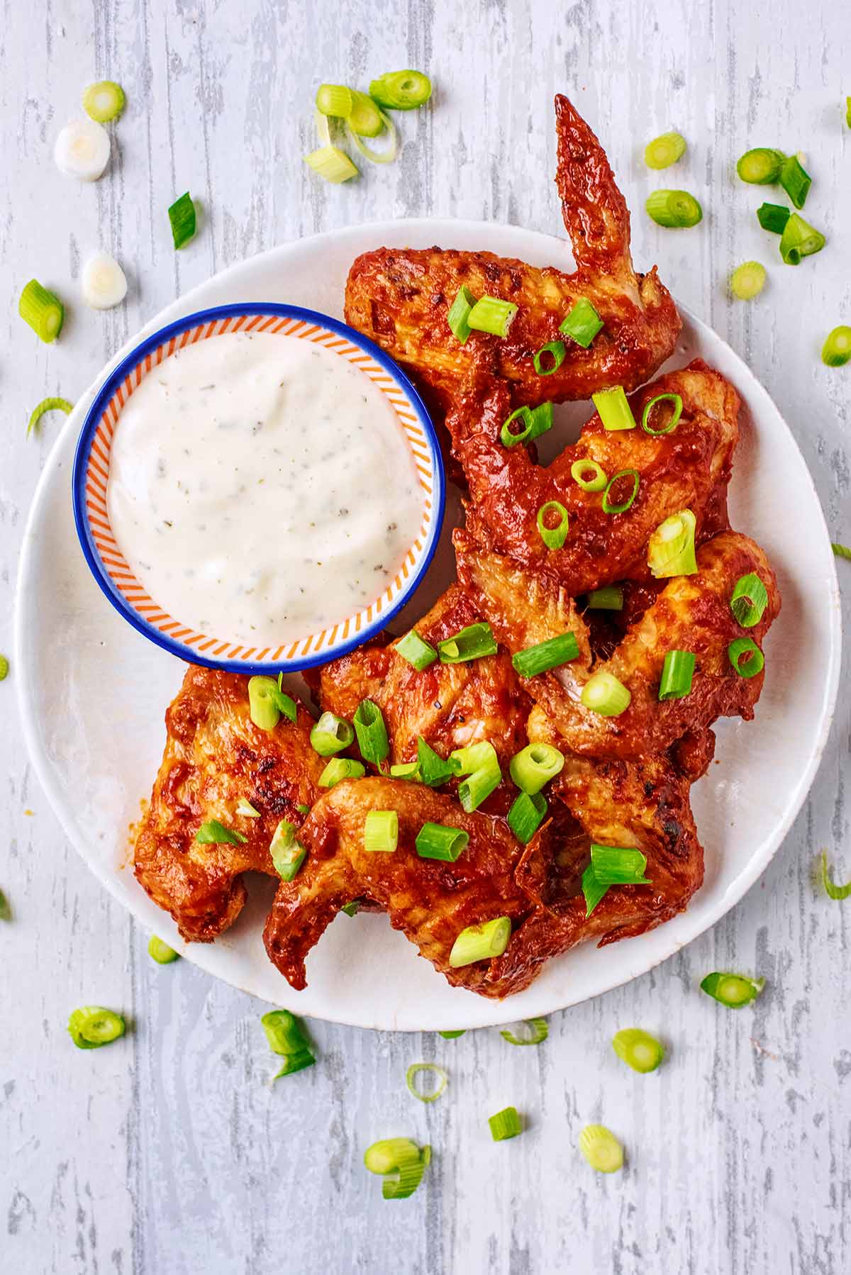 A plate of cooked chicken wings with a small bowl of dip.
