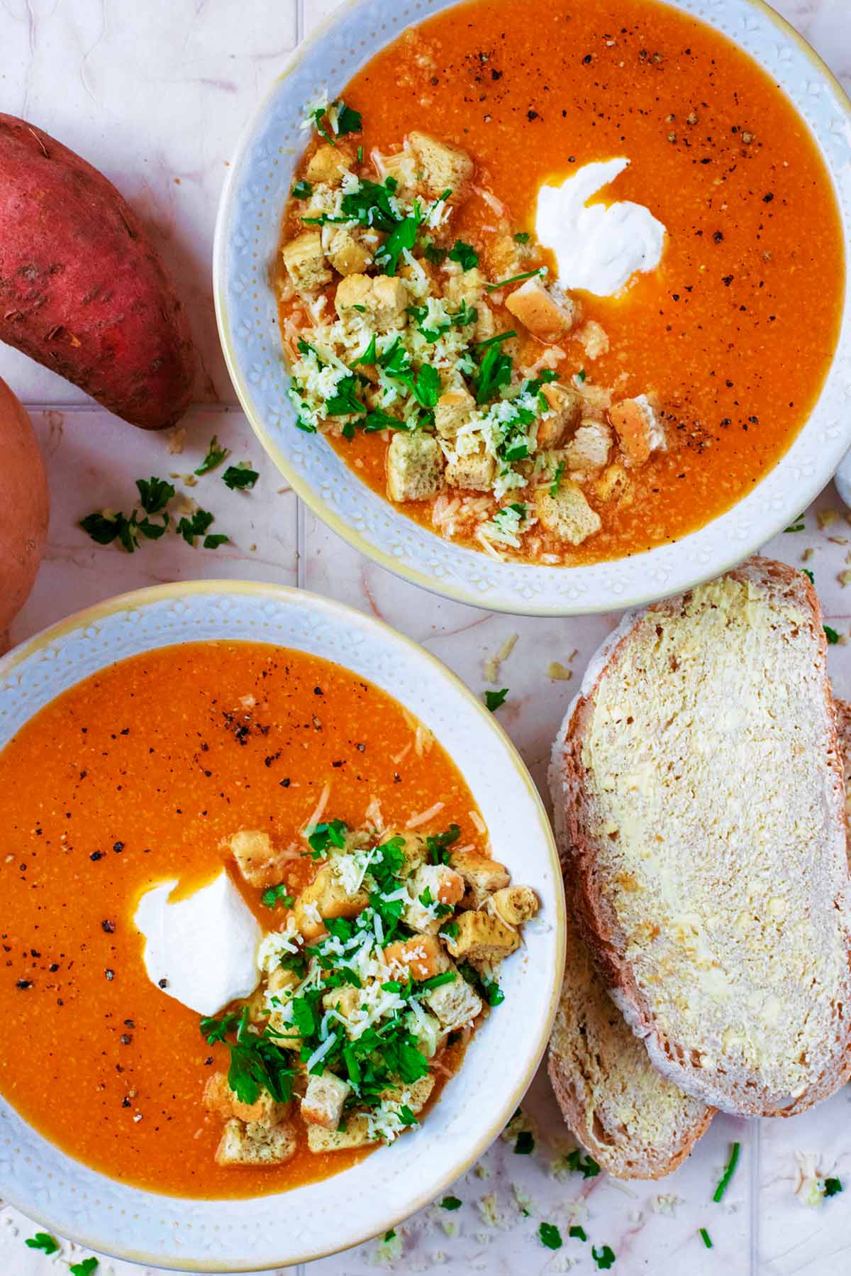 Two bowls of orange coloured soup next to some buttered bread.