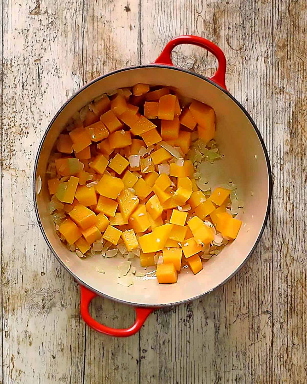 Sweet potato and butternut squash chunks cooking in a pan with chopped onion.