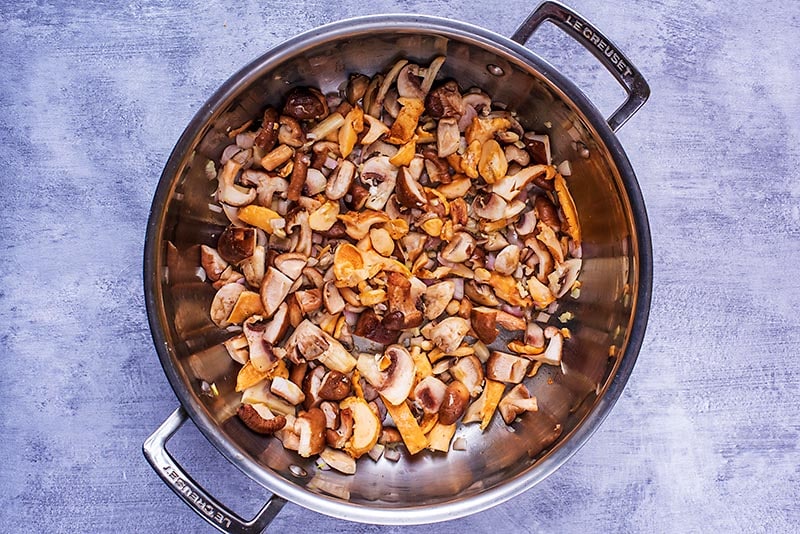 Sliced mushrooms cooking in a large pan.