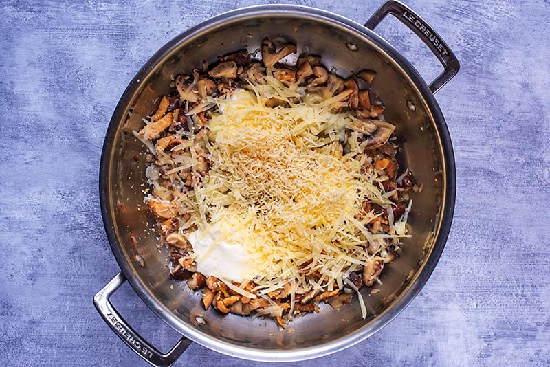 A large pan containing cooked mushrooms, cream and grated cheese.