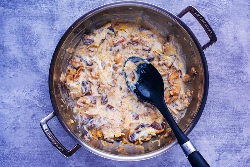 A creamy mushroom sauce cooking in a large pan.