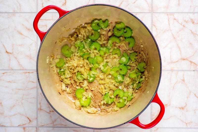 A large red pan containing celery, crushed garlic and shallots.