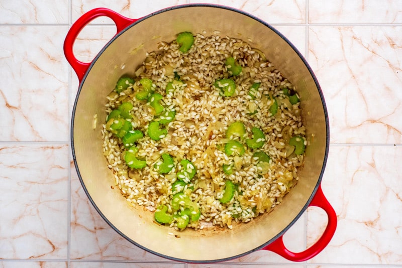 A large red pan containing celery, shallots and risotto rice.