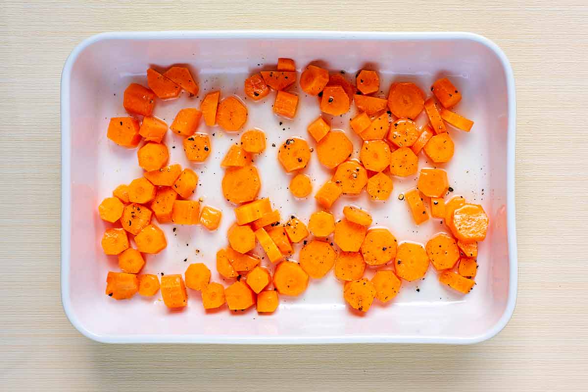 Sliced carrots, oil and seasoning in a baking dish.