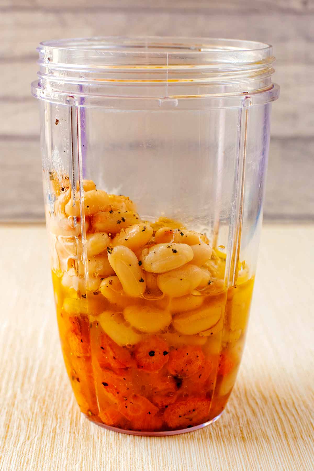 A blender jug containing beans, roasted carrots, oil and tahini.