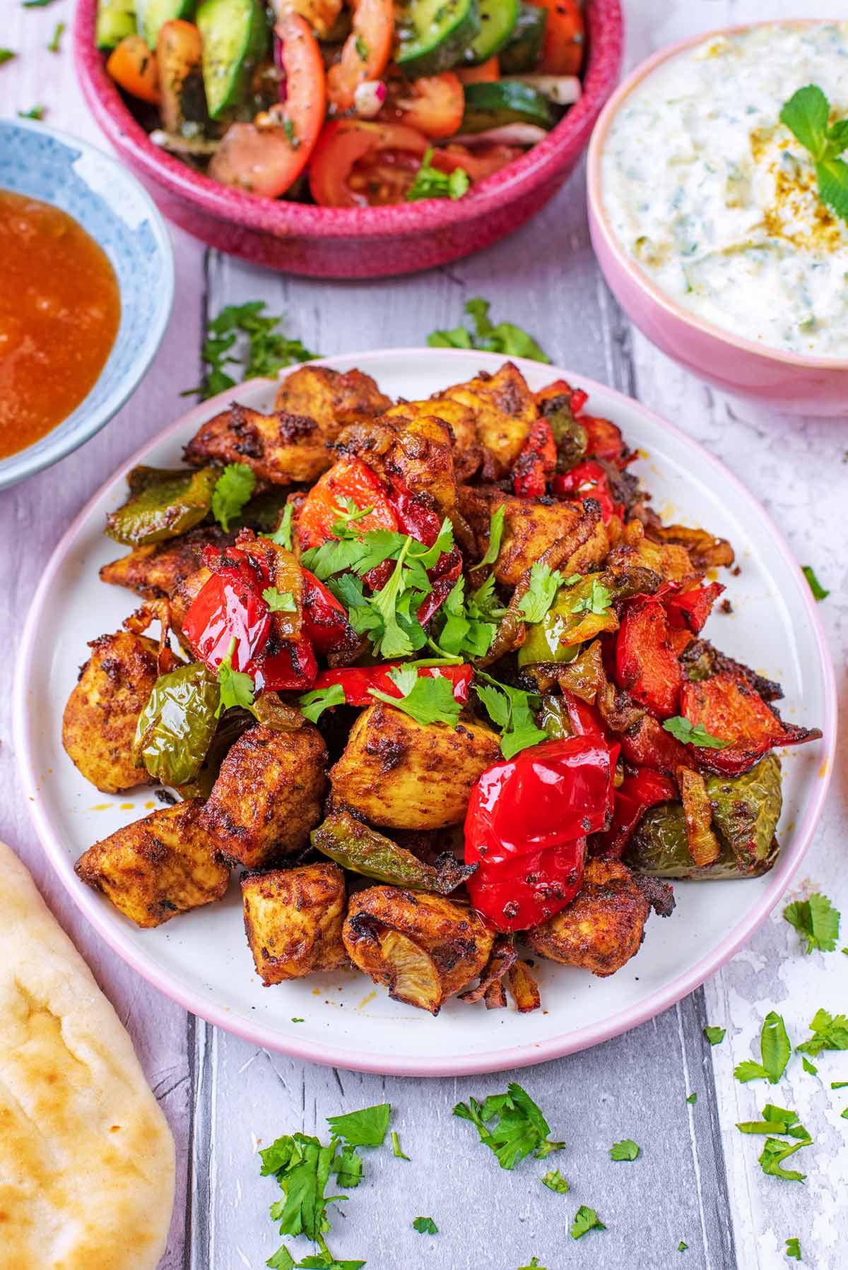 A pile of chicken tikka chunks, on a white plate with cooked peppers.