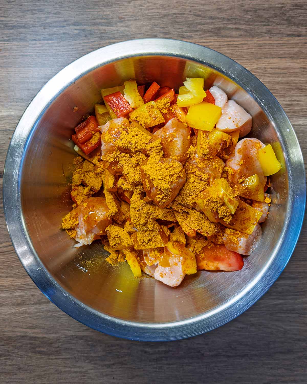 A mixing bowl containing chicken chunks, chopped peppers, onion, tomatoes and seasoning.