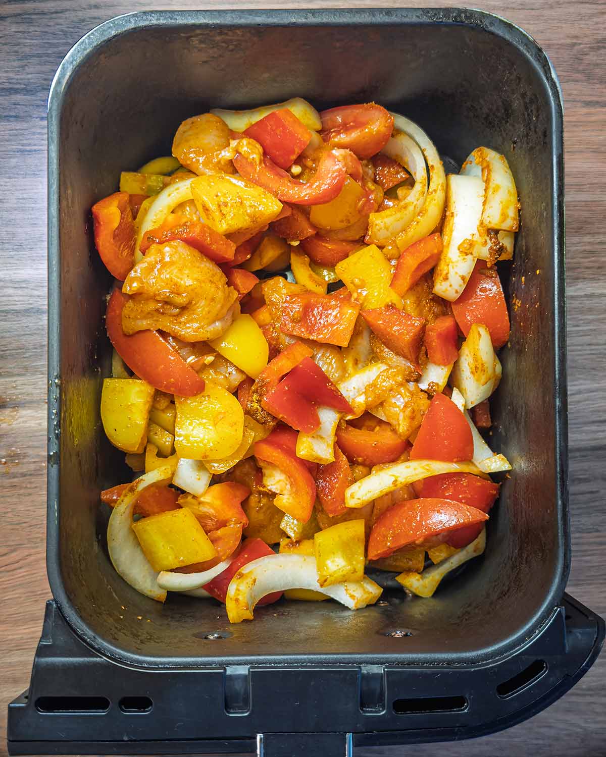 Seasoned chicken chunks and vegetables in an air fryer basket.