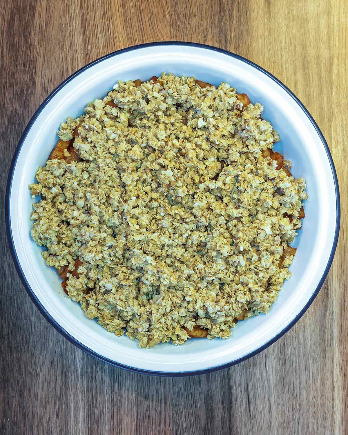 The cooked apples in a baking dish topped with the oat mixture.