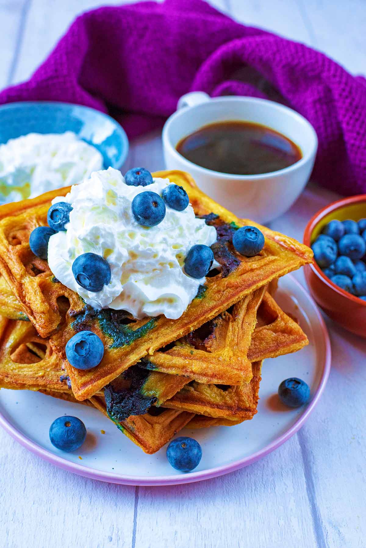 A plate of waffles topped with whipped cream and blueberries.