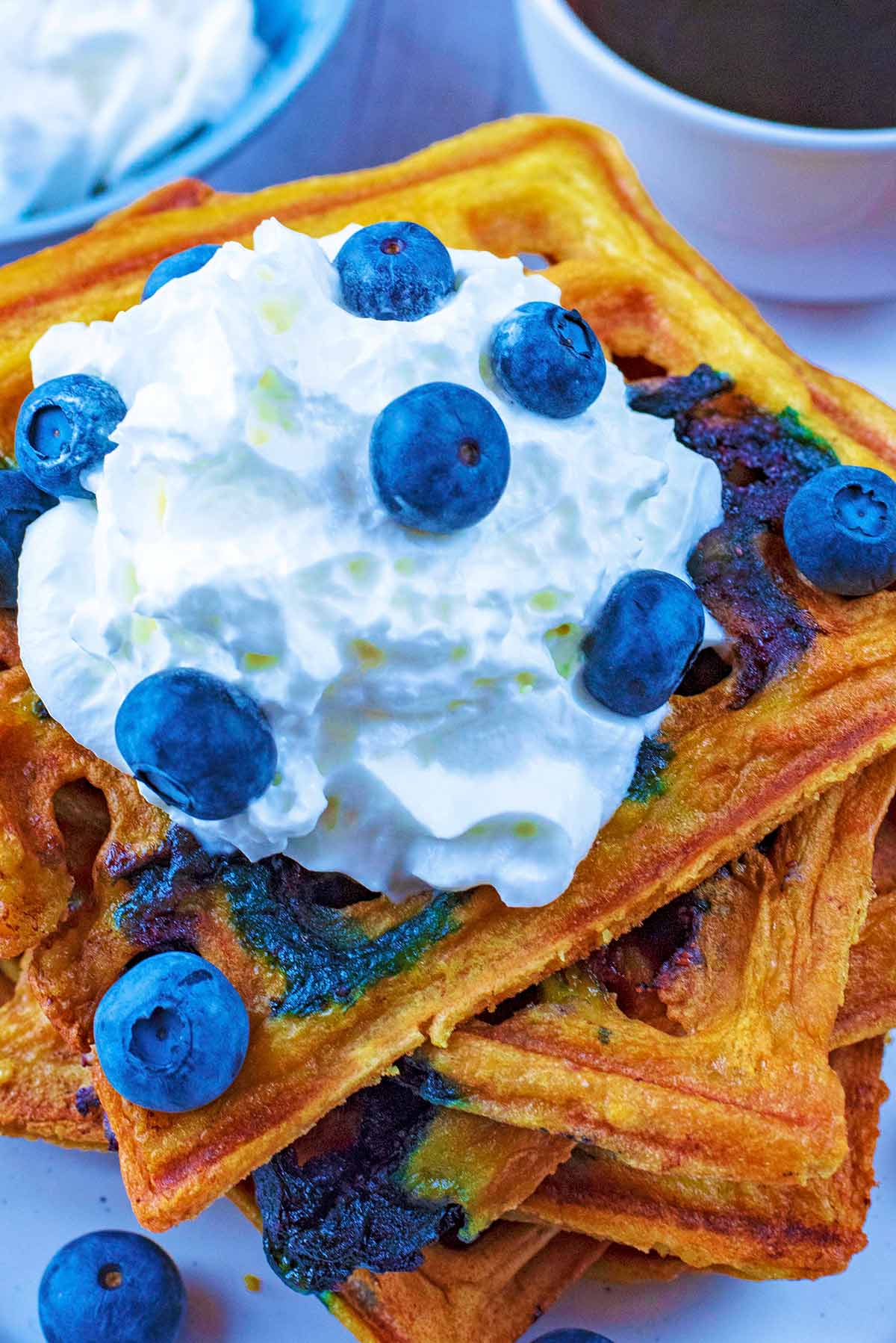 A stack of waffles with a dollop of cream and scattered blueberries.